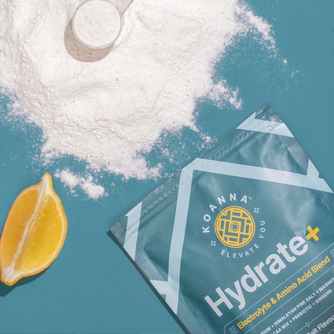 A poured out Hydrate+ package with white powder, measuring spoon and lemon wedge on a blue background.