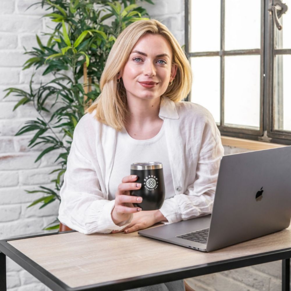 Blonde woman sitting in front of her laptop and holding Elevate cup by Koanna.